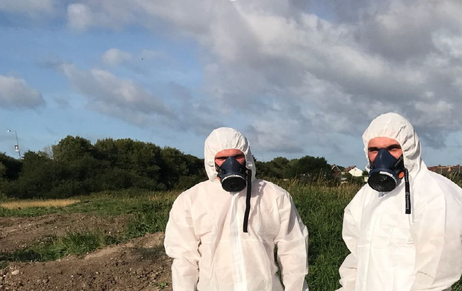 Two men outside with masks and coveralls
